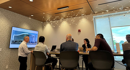 Group of individuals sitting at a table with a presenter standing in front