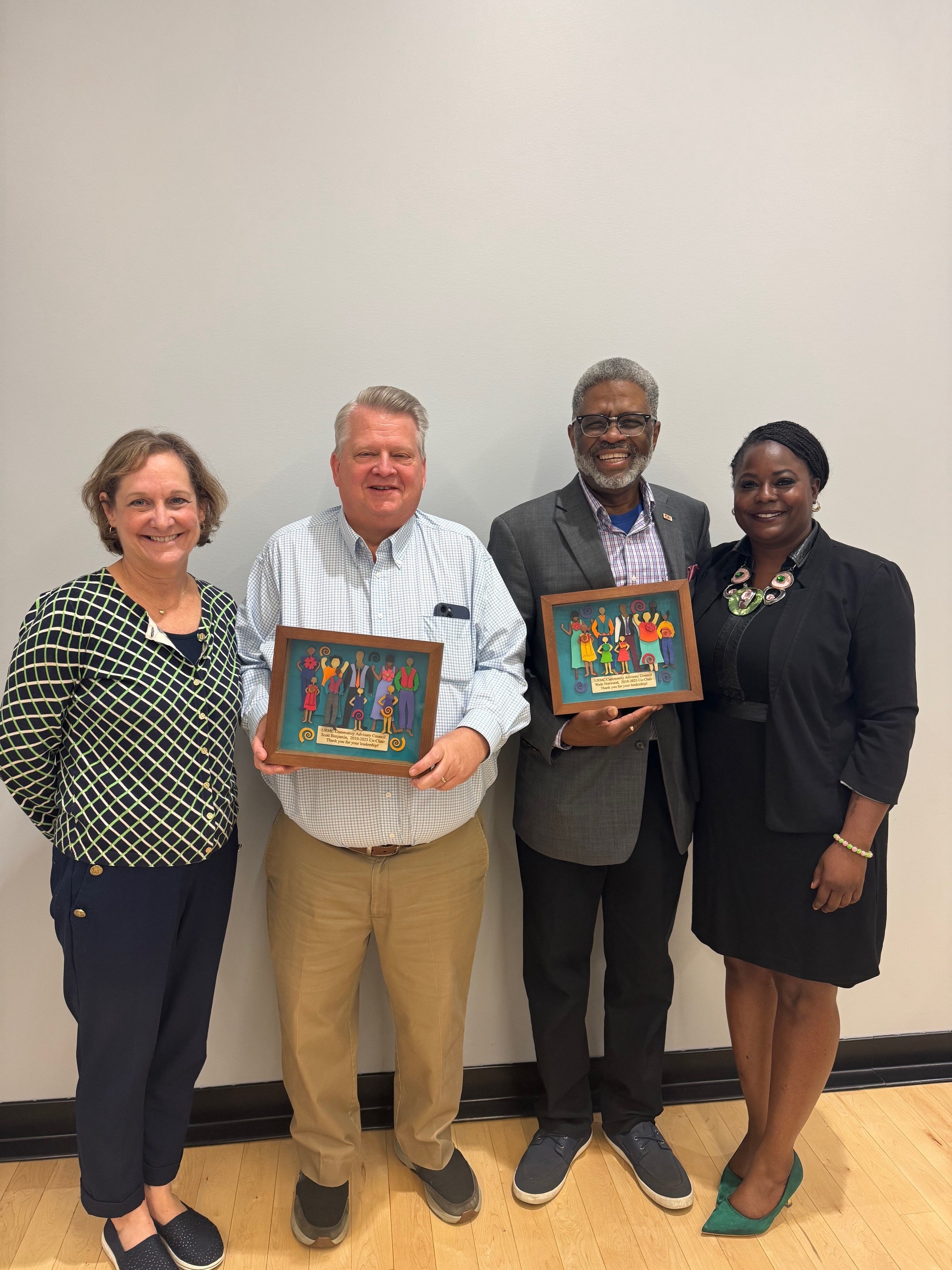 Four people standing together, with two in middle holding award plaques.