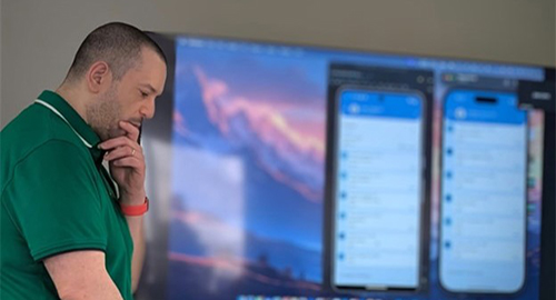 Image of a man standing in front of a room looking down at a computer screen while presenting